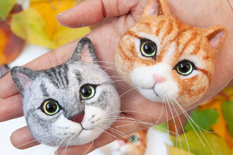 Hand holding two cat-shaped toys with a blurred autumn leaf background